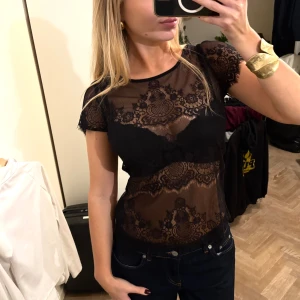 Svart spetsblus från Hallhuber Donna - Supersnygg svart blus i transparent spets från Hallhuber Donna. Blusen har korta ärmar, rund halsringning och ett detaljerat spetsmönster med fina kanter. Perfekt att styla med jeans eller kjol för en cool look.