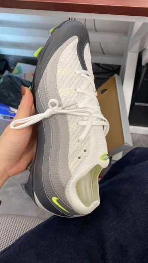 Nike Air fotbollsskor vit/grå - Nike Air fotbollsskor med snygg design i vitt och grått, detaljer i neongult och svart. Skon har snörning, stickad ovandel och inslag av syntet och skinn. Platt sula med dobbar för gräsplan. Perfekt för dig som vill ha stil på planen.