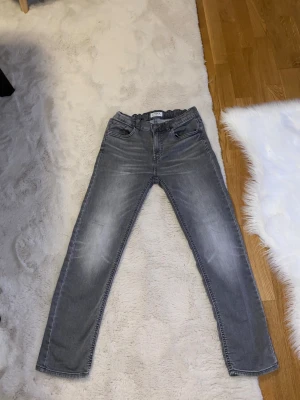 Grå jeans med resårmidja - Snygga grå jeans från Lindex med resår i midjan och klassisk femficksdesign. Jeansen har en lätt tvättad look och raka ben. Perfekta för dig som gillar en avslappnad stil med bekväm passform. De bra för skolan är väldigt skön och bra material. Har haft på mig den en gång och det var för skolfoto sen des har jag inte haft på mig den. Den e helt ren.