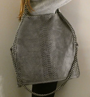 Väska  - Stor grå väska med kedja, har två kortare kedjor och en längre. Perfekt som skolväska, två fack finns inuti och en dragkedja för att stänga väskan