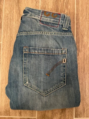 Blåa dondup jeans - Snygga blå dondup jeans med klassisk femficksdesign och kontrastsömmar. Jeansen har en ljus tvätt och snygg design på bakfickan med de klassiska dondup märket. Perfekt för dig som gillar en avslappnad och stilren look.