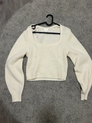 Vit croppad stickad topp från H&M - Säljer en vit croppad stickad topp från H&M med fyrkantig halsringning och långa ärmar. Toppen har en ribbad struktur och är mjuk och skön, perfekt för att ge din outfit en chill vibe. Passar dig som gillar enkla och stilrena plagg.