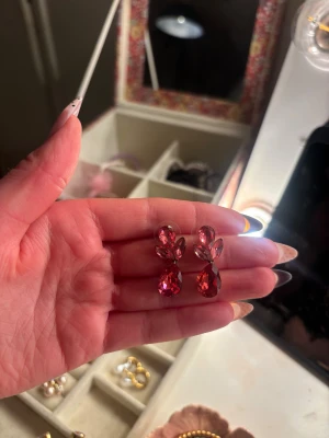 Rosa statement örhängen med stenar - Säljer ett par glittriga statement örhängen i silverfärgad metall med stora rosa stenar i droppform och marquiseform. Örhängena har en elegant design och ger en lyxig känsla till din look.