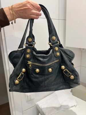Balenciaga svart handväska med guldknappar - Balenciaga city bag. Super fint skick för att vara vintage. Lite slitningar på kanterna men i övrigt jätte fin. Har inte kvitto eller dustbag dessvärre!💞💞💞 hör av er för frågor🫶🏼 finns på vestiare oxå där äkthets kontroller görs! 