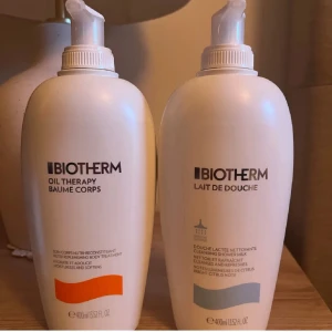 Biotherm Oil Therapy & Lait de Douche - Två stora pumpflaskor från Biotherm, Oil Therapy Baume Corps och Lait de Douche. Båda är vita med stilren design, 400 ml vardera. Oil Therapy har en orange detalj och Lait de Douche en gråblå. Perfekt för dig som gillar lyxiga kroppsvårdsprodukter. 