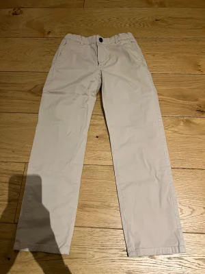 Beiga Chinos - Beiga chinos i storlek 140. Bra passform och i mycket fint skick – inga fläckar eller hål. Bekväma och lätta att röra sig i.