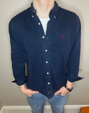 Mörkblå skjorta från Polo Ralph Lauren - Klassisk mörkblå skjorta från Polo Ralph Lauren i 100% bomull. Skjortan har button-down krage, vita knappar och den ikoniska röda broderade loggan på bröstet. Perfekt passform och tidlös stil som funkar till allt. Det är storlek 95 men passar S/Xs. Pris är diskuterbart vid snabb affär. 