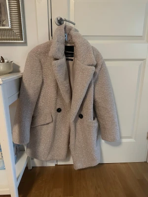 Beige teddyjacka Pull&Bear XS - Säljer en beige teddyjacka från Pull&Bear i storlek XS. Jackan har bred krage, två stora fickor framtill och stängs med två svarta knappar. Den är fluffig och har en loose passform, perfekt för kalla dagar. Materialet är mjukt och ger en mysig vibe. Har använt den unde vintern och den värmer extremt mycket! 