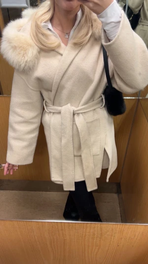 Beige kappa med pälsdetalj huva  - Säljer en beige kappa med avtagbar päls på luvan    , vet inte vilket märke då jag har fått den i present för cirka ett år sen. Den är sparsamt använd med mycket fin päls och material, storlek xs. Säljer den då den inte kommer till användning längre💕💕