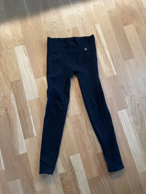 Svarta ribbade leggings från Calzedonia - Svarta leggings från Calzedonia i ribbad, stretchig syntetmix. Hög midja och tight passform som sitter snyggt och bekvämt. Perfekta för dig som gillar en clean och sportig look. Diskret logga framtill i midjan.
