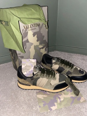 Valentino Garavani Rockrunner sneakers - Säljer ett par Valentino Garavani Rockrunner sneakers med camouflagemönster i grönt, beige och svart. Skorna har snörning, platt sula med gummidetaljer och ovandel i mocka och textil. Ikonisk logga på plösen och coola nitar på hälen. Perfekt för dig som gillar streetstyle.