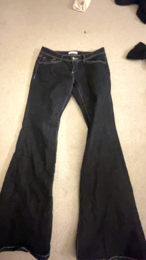 Bootcut jeans från Gina Tricot, svart - Svarta bootcut jeans från Gina Tricot i modellen 'perfect jeans'. Snygg kontrastsöm och klassisk femficksdesign. Jeansen har låg midja och är tillverkade i ett stretchigt denimtyg som sitter skönt och ger en schysst siluett.