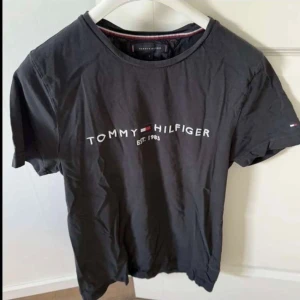 Svart Tommy Hilfiger t-shirt S - Svart t-shirt från Tommy Hilfiger i ekologisk bomull. Klassisk rund halsringning och tryckt logga framtill med texten 'Tommy Hilfiger Est. 1985'. Kortärmad och stilren design, perfekt till jeans eller shorts.