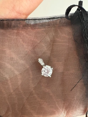 Silver hängsmycke med gnistrande sten - Snyggt hängsmycke i äkta silver (925) med en stor rund gnistrande klar sten i mitten och små stenar på fästet. Perfekt att bära i en kedja för att ge din look extra bling. Stenarna är slipade för maximal glans och hängsmycket har en modern, stilren design.