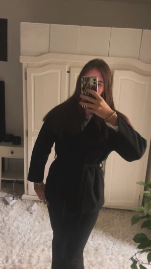 Svart kappa från Missay - Säljer en svart kappa med omlottmodell och bälte i midjan. Jackan har lång ärm och en stilren, enkel design.