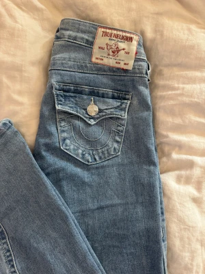 True Religion Joey ljusblå flare jeans - Säljer fina true religon jeans i mycket bra skick som är använda 3-4 gånger och tvättade två gånger. Supersnygga och sitter perfekt på kroppen. De är i storlek 23 (internationell storlek) vilket motsvarar och passar perfekt på dig som vanligtvis har storlek 32 i byxor. Jag skulle säga att de är lite längre än vad andra byxor är. De är köpta för 1300kr.