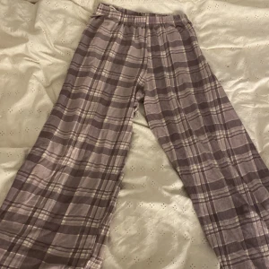 Lila rutiga byxor från H&M - Säljer ett par lila rutiga byxor från H&M i storlek 146/152. Byxorna har elastisk midja och är tillverkade i mjuk bomull. De har ett loose fit och ett klassiskt rutmönster i olika lila nyanser. Perfekta för chill dagar hemma.