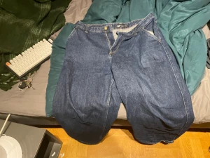Blåa wide jeans från pull&bear - Säljer ett par mörkblå jeans från pull&bear med bred passform och raka ben. Klassisk femficksmodell med guldfärgad knapp och synliga sömmar. Jeansen har en loose och avslappnad stil, perfekta för dig som gillar streetwear och oversized look.