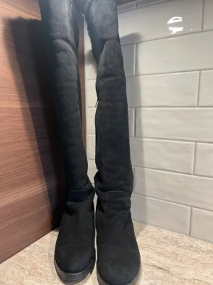 Svarta mockastövlar Marzio strl 36,5 - Snygga svarta stövlar i mocka med platt sula och rund tå. De är höga, går över knäet och har en dragkedja på insidan. Insidan är fodrad med pälsfoder för extra värme. Perfekta för kalla dagar och ger en stilren look till din outfit. Köpta på Blocket nyligen men var för små för mig ( jag är liten 37:a). Enl ägaren endast använda 1 ggn. Jag har endast provat dem inomhus. Nypris Marzio vintern -24, 7500kr. Fantastiska stövlar som passar en normal 36:a.