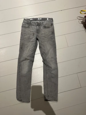 Grå slim jeans från Jack & Jones - Slim fit jeans från Jack & Jones i snygg grå tvätt med klassisk femficksdesign. Jeansen har raka ben, normal midja och subtila slitningar framtill för en cool look. Materialet är mjukt och stretchigt denim som sitter skönt hela dagen.