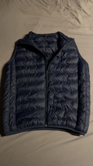 Mörkblå dunväst från Lawrence Grey - Snygg mörkblå dunväst från Lawrence Grey med lättviktsfyllning av återvunnet syntetdun. Västen har quiltad design, dragkedja framtill och hög krage. Perfekt att slänga över en hoodie eller tröja för extra värme.