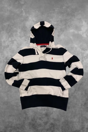 Vintage Ralph Lauren Hoodie - Snygg hoodie från Polo Ralph Lauren i storlek XS, dock passar den som en storlek S. Tröjan har breda marinblå och vita ränder, huva med snörning och en röd broderad logga på bröstet. Tillverkad i mjuk bomull med känguruficka framtill och ribbade muddar vid ärmslut och nederkant.