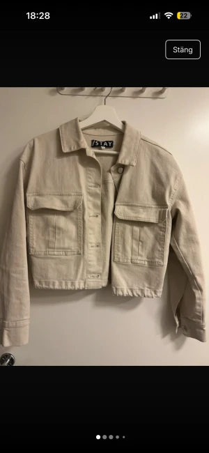 Beige jeansjacka från Stay - Snygg beige jeansjacka från Stay med croppad passform och stora bröstfickor. Jackan har klassisk krage, knappar framtill och dragsko i nederkant. Perfekt för dig som gillar en stilren och avslappnad look.