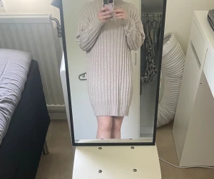 Beige ribbstickad klänning - Mysig beige stickad klänning med ribbat mönster och polokrage. Långa ärmar och mjukt material som känns skönt mot huden. Perfekt för dig som gillar en enkel men stilren look.