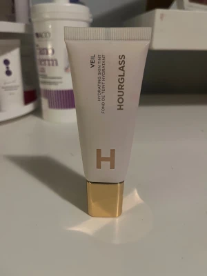Hourglass Veil Hydrating Skin Tint - Hourglass Veil Hydrating Skin Tint i en stilren vit tub med guldig kork. Ger en lätt täckning och återfuktar huden samtidigt. Perfekt för dig som vill ha en naturlig finish och glow. Innehåller 35 ml och är enkel att applicera med fingrar eller borste.