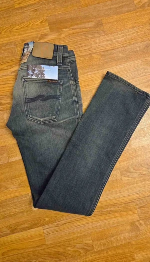 Nudie Jeans Slim Jim 29/34 - Mörkblå jeans från Nudie Jeans, modell Slim Jim straight tubeleg. Klassisk femficksdesign med snygga slitningar och kontrastsömmar. Rak passform med normal midja och läderpatch bak. Perfekt för dig som gillar stilrena och tidlösa jeans.
