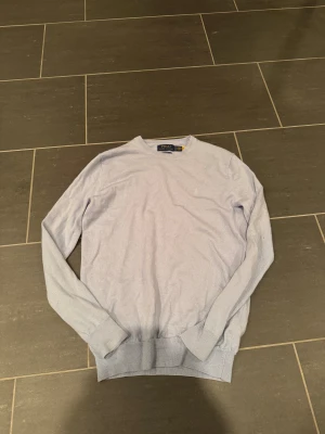  Polo Ralph Lauren - Snygg ljuslila stickad tröja från Polo Ralph Lauren i slim fit. Tröjan har rund hals och långa ärmar, med diskret broderad logga på bröstet. Perfekt för dig som gillar klassisk och stilren design med en soft vibe.