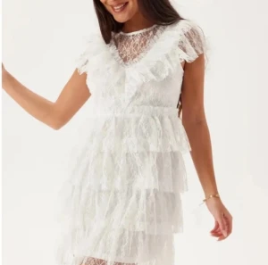 Klänning - Supersöt vit kortklänning med flera lager volanger och spetsdetaljer. Klänningen har v-ringad hals, transparent spets upptill och korta ärmar. Perfekt för dig som gillar romantisk och feminin stil. Passar till student eller midsommar. Endast använd en gång!!