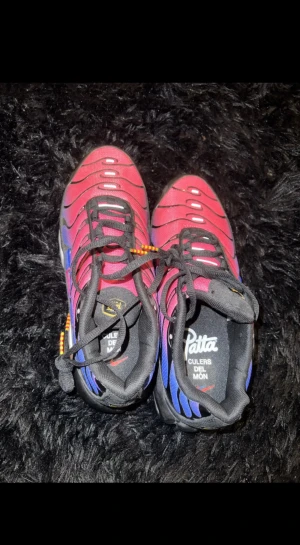 Nike x Patta Air Max Plus Culers Del Mon - Nike Air Max Plus i samarbete med Patta, modellen 'Culers Del Mon'. Snygg gradient i röd och blå med svarta detaljer och orange inslag på sulan. Skorna har snörning, platt sula och rund tå. Materialet är syntet och mesh, med Patta-logga på innersulan.