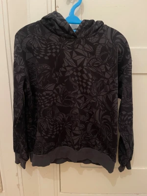 Svart hoodie med grafiskt mönster Lindex - Svart hoodie från Lindex med grafiskt mönster i grått. Tröjan har huva, ribbade muddar och är långärmad. 