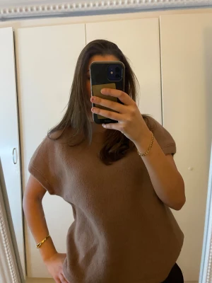 Brun stickad topp med korta ärmar - Säljer en brun stickad topp med korta ärmar och rund hals. Modellen är loose fit och har en enkel, stilren design utan mönster eller detaljer. Perfekt för dig som gillar en chill och avslappnad look.