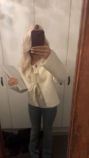 Vit stickad kofta med knytband - Superfin vit stickad kofta med breda ärmar och två stora knytband framtill. Koftan har en rak, lite loose passform och är ribbstickad för extra mysig känsla. Perfekt att slänga på sig över ett linne eller t-shirt.