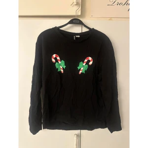 Svart jultröja med polkagrisar H&M - Svart långärmad tröja från H&M Divided med två polkagrisar och gröna rosetter tryckta på bröstet. Perfekt för dig som vill sticka ut på julens alla tillfällen. Mjuk bomullskvalitet och rund halsringning. 