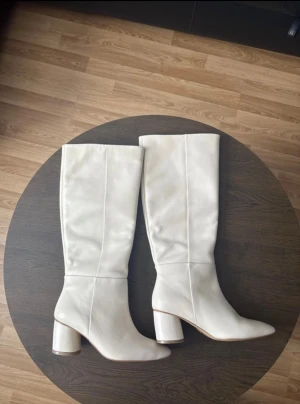 Vita höga stövlar med klack - Snygga vita stövlar med rund tå och stabil blockklack. Stövlarna är tillverkade i mjukt skinn. Nyskick utan prislapp, skorna är ej använda utan bara testade. 