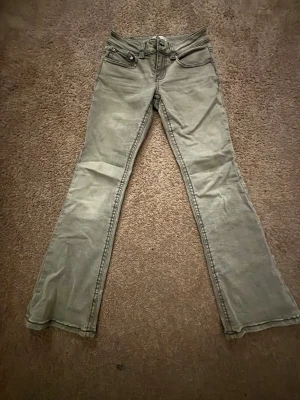 Grå bootcut jeans från Perfect Jeans - Snygga grå jeans från Perfect Jeans i bootcut-modell med klassiska fem fickor och coola bakfickor med lock och knapp. Jeansen har normal passform och är tillverkade i mjukt jeanstyg. Perfekt för dig som gillar retrovibbar och vill sticka ut.