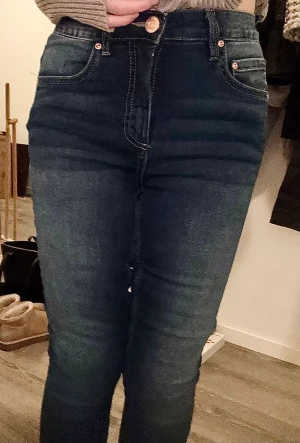 Mörkblå skinny jeans med hög midja - Mörkblå skinny jeans med hög midja och klassisk femficksdesign. Jeansen har kontrastsömmar och kopparfärgade nitar vid fickorna.