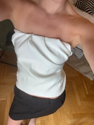 Vit bandeau tubtopp Zara - Säljer en vit tubtopp med snygga draperingar. Toppen är axelbandslös och har en stilren, modern look som är perfekt för dig som gillar minimalistisk stil. Helt ny, aldrig använd.