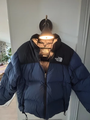 Blå och svart pufferjacka North Face - Säljer min The North Face 1996 Retro Nuptse i färgen Summit Navy/TNF Black, storlek M. Använd en vintersäsong och i mycket fint skick. Klassisk boxig passform, 700-fill dun, slitstarkt ripstop-tyg och packbar huva. Varm, lätt och ikonisk modell utan skador eller slitage. Perfekt för både vardagligt- och vinterväder. Hör av dig för fler bilder eller info!