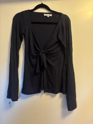 Svart långärmad topp med knyt - Svart långärmad topp från Design by si med djup v-ringning och snygg knytning framtill. Tunn och mjuk i materialet. 