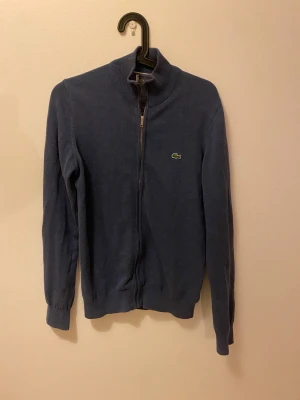 Lacoste zip - Snygg marinblå kofta från Lacoste med klassisk krokodillogga på bröstet. Tröjan är stickad och i väldigt mjukt material, 100% bomull. Förutom att lappen i nacken är bortklippt är den i bra skick. Kontakta mig om frågor!🐊😃