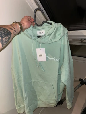 Mintgrön hoodie från Nikben - Snygg mintgrön hoodie från Nikben med stor vit logga på ryggen och texten 'That's it!' på bröstet. Tröjan har huva med snörning, känguruficka och långa ärmar. Perfekt för chill dagar och streetstyle. Materialet är mjuk bomull för skön komfort. Tröjan är helt ny.