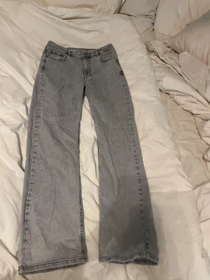 Grå mid wide jeans - Säljer ett par grå jeans med midwaist och wide fit. Klassisk femficksmodell med raka ben och snyggt slitna detaljer. Jeansen är tillverkade i jeansmaterial och har en neutral grå färg som passar till allt. Perfekt för dig som gillar avslappnad stil.