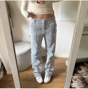 Randiga blåvita raka byxor - Jag är 175, då dem är väldigt långa. Säljer ett par snygga blåvita byxor med smala vertikala ränder. De har normal passform, raka ben och midwaist. Byxorna har fickor fram och bak samt hällor för bälte. Perfekta för dig som gillar en chill och stilren look.
