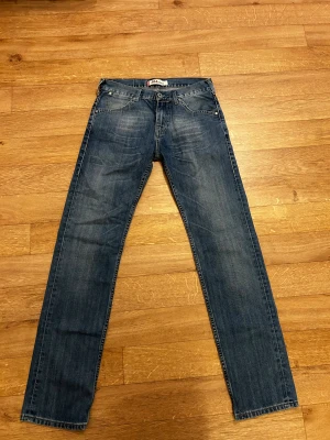 Levi's 504 straight jeans blå - Säljer ett par klassiska Levi's 504 straight jeans i mörkblå tvätt med snygga slitningar. Modellen har fem fickor, normal passform och raka ben. Jeansen är tillverkade i slitstarkt bomullsdenim och har den ikoniska röda Levi's-taggen på bakfickan.