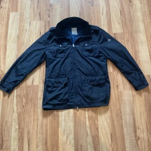 Marinblå vindjacka från J.Lindeberg - Säljer en marinblå J.Lindeberg jacka i ett helt perfekt skick inga synliga defekter eller så. En tunn jacka perfekt att ha under våren och hösten. Använd ett fåtal gånger.