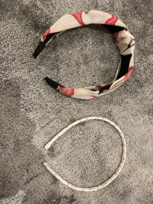 Två diadem, ett knut och ett prickigt - Säljer två snygga diadem! Ett bredare diadem med knut i ljusbeige, rött och svart mönster, tillverkat i mjukt tyg. Det andra är smalare, vitt med små guldprickar och hjärtan, också i tyg. Perfekt för att ge din look lite extra stil.